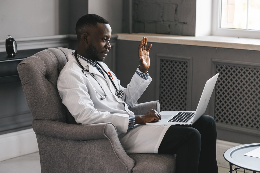 Male doctor sitting in chair waving to laptop